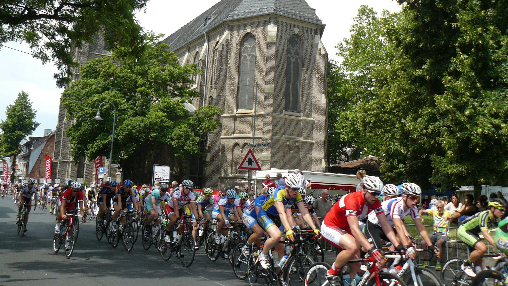 Rennradfahrer fahren im Pulk, im Hintergrund ist eine Kirche zu sehen.