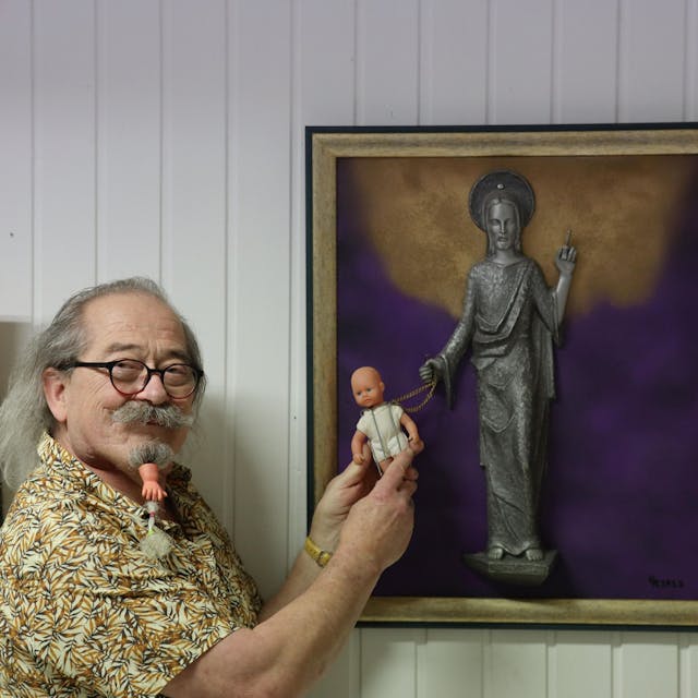 Uwe Rhiem hält eine Puppe vor ein Bild mit einer Christusfigur.