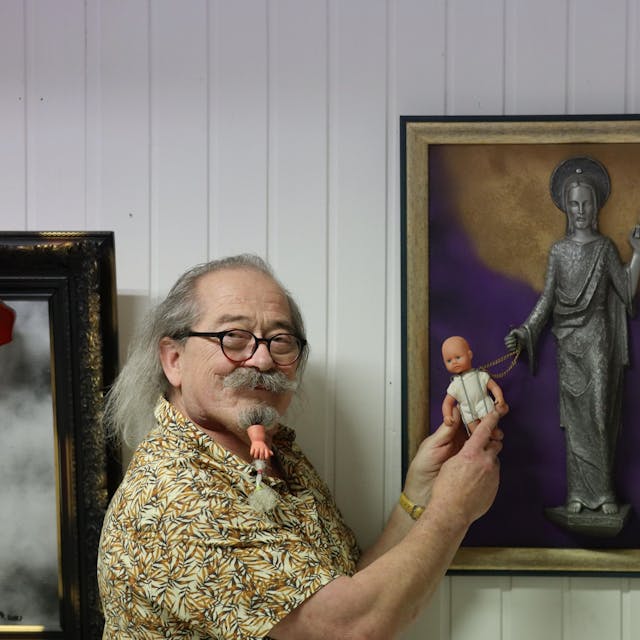 Uwe Rhiem hält eine Puppe vor ein Bild mit einer Christusfigur.