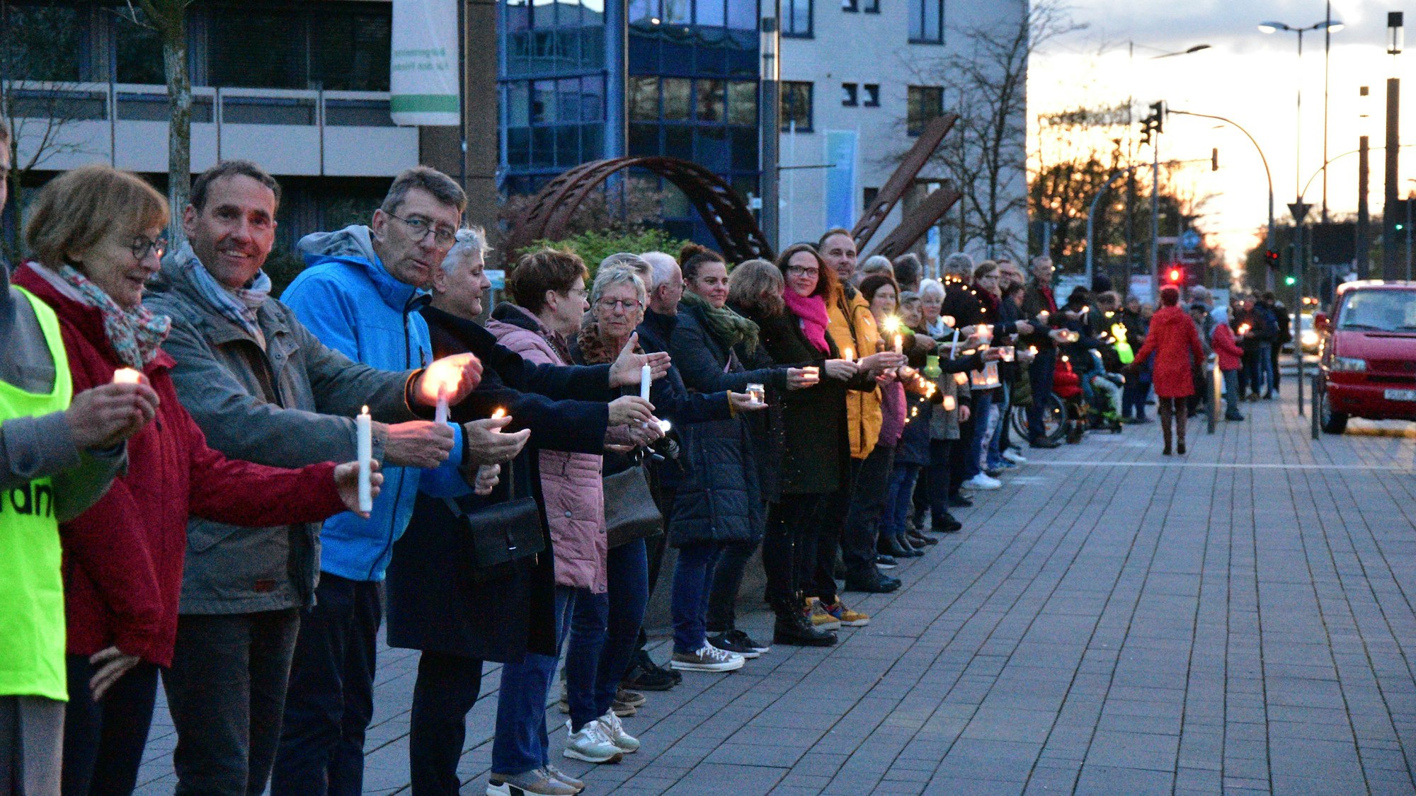 Menschen stehen auf dem Gehweg vor einem Verwaltungsgebäude. Sie tragen Kerzen in den den Händen.