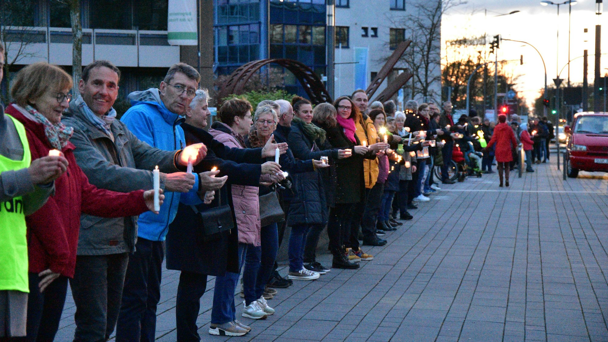 Eine lange Reihe von Menschen steht nebeneinander auf einem Gehweg; sie tragen Kerzen in ihren Händen.