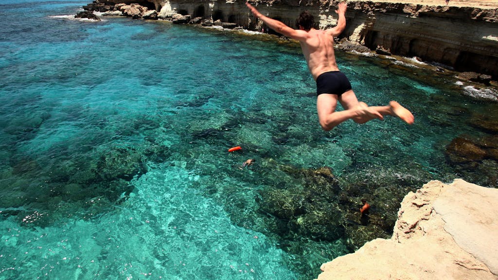 Ein Mann springt am Cape Greco auf Zypern ins Meer.