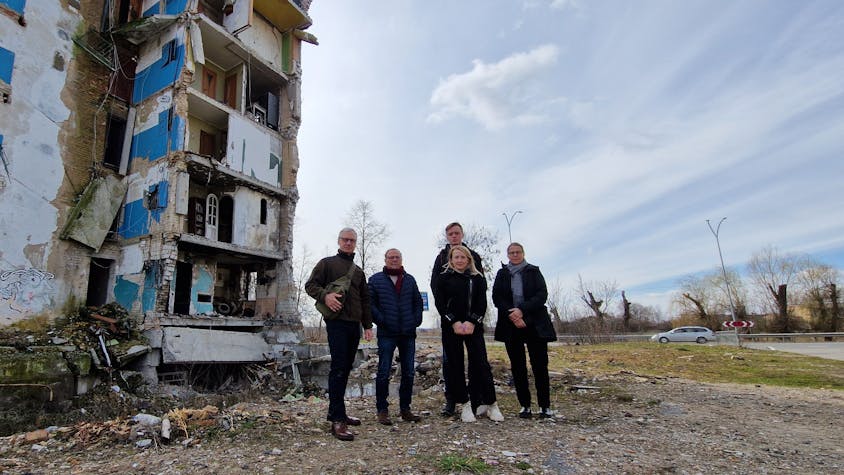 Das Foto zeigt ein Gruppenbild vor einem schwer beschädigten Wohnblock.