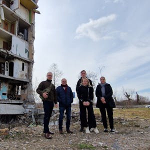 Das Foto zeigt ein Gruppenbild vor einem schwer beschädigten Wohnblock.