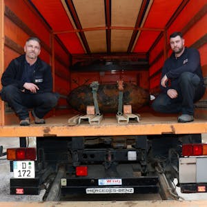 Zwei Männer in Dienstkleidung im Innenraum eines Lastwagens, in ihrer Mitte ist eine entschärfte Bombe festgeschnallt