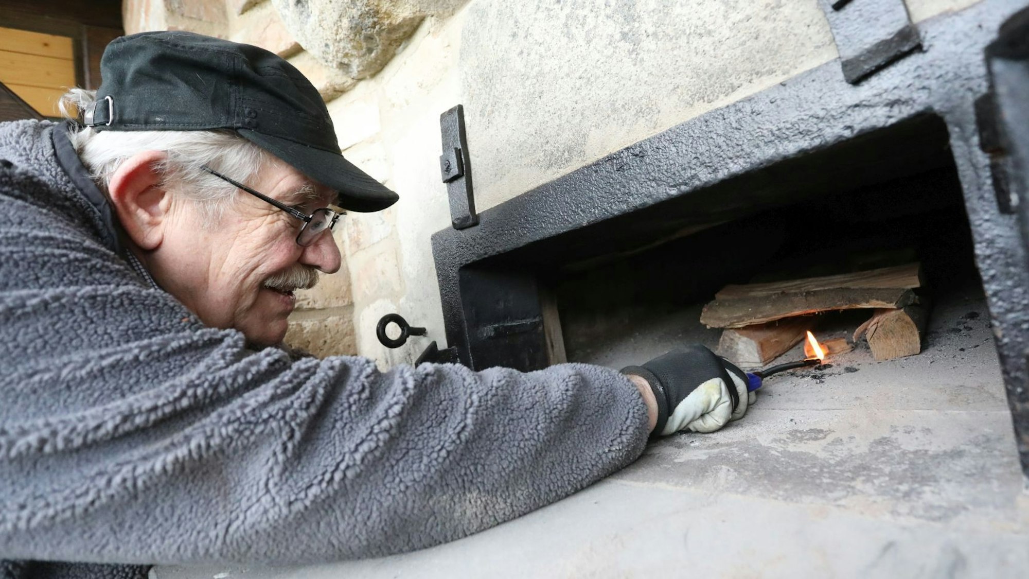 Ein Mann mit Basecap hält eine Flamme unter einen kleinen Holzscheit.