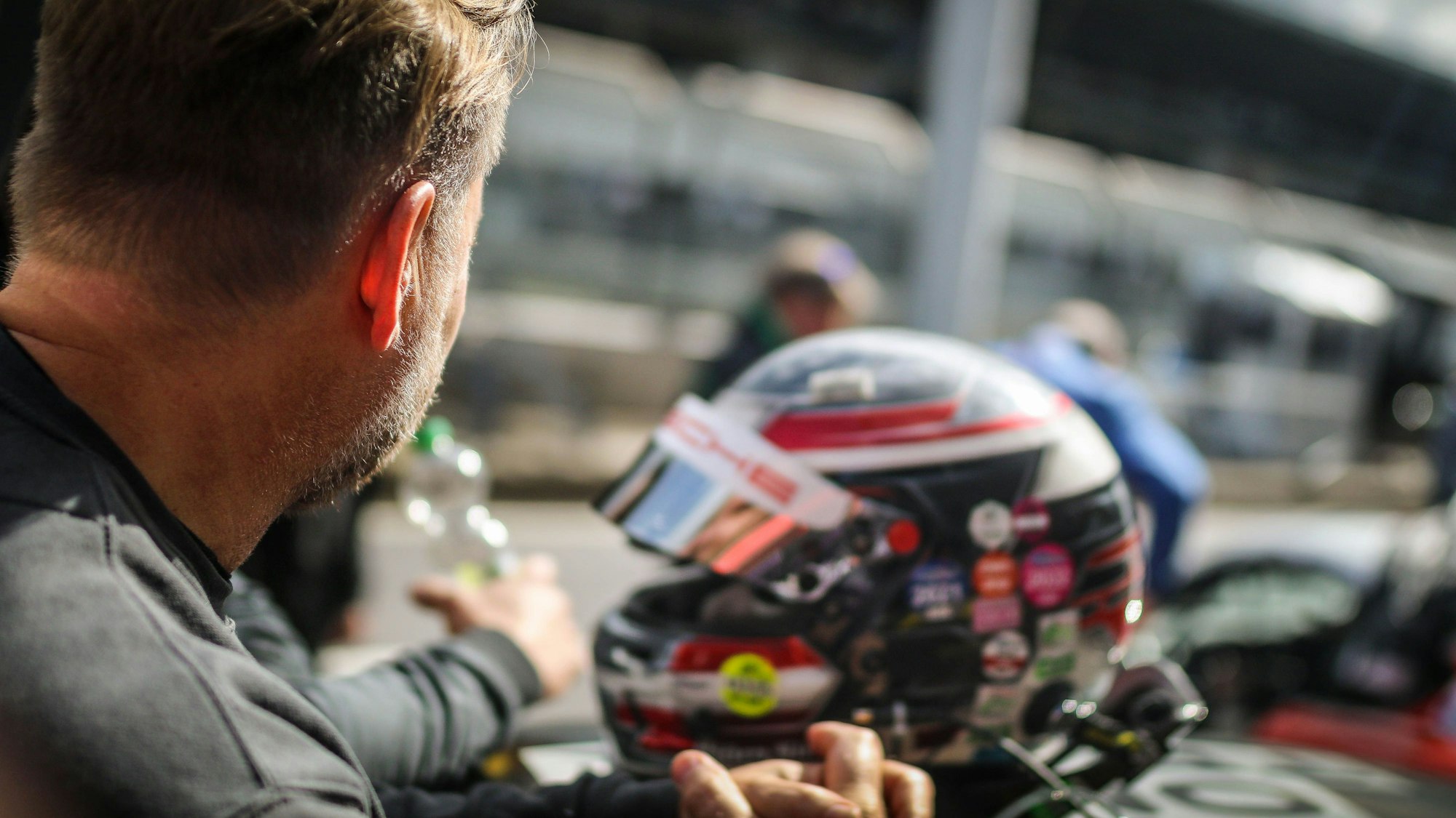 Ein Rennfahrer schaut am Nürburgring in Richtung Boxengasse, im Hintergrund ein Helm.