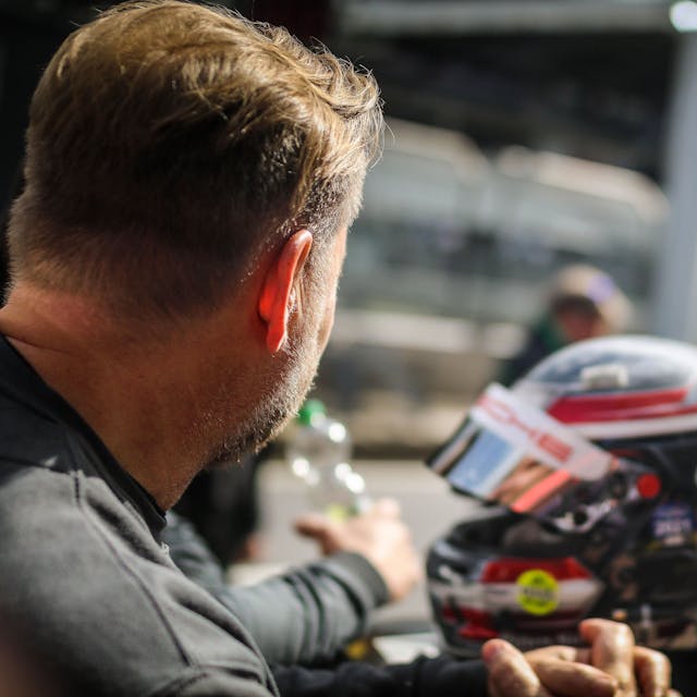 Ein Rennfahrer schaut am Nürburgring in Richtung Boxengasse, im Hintergrund ein Helm.