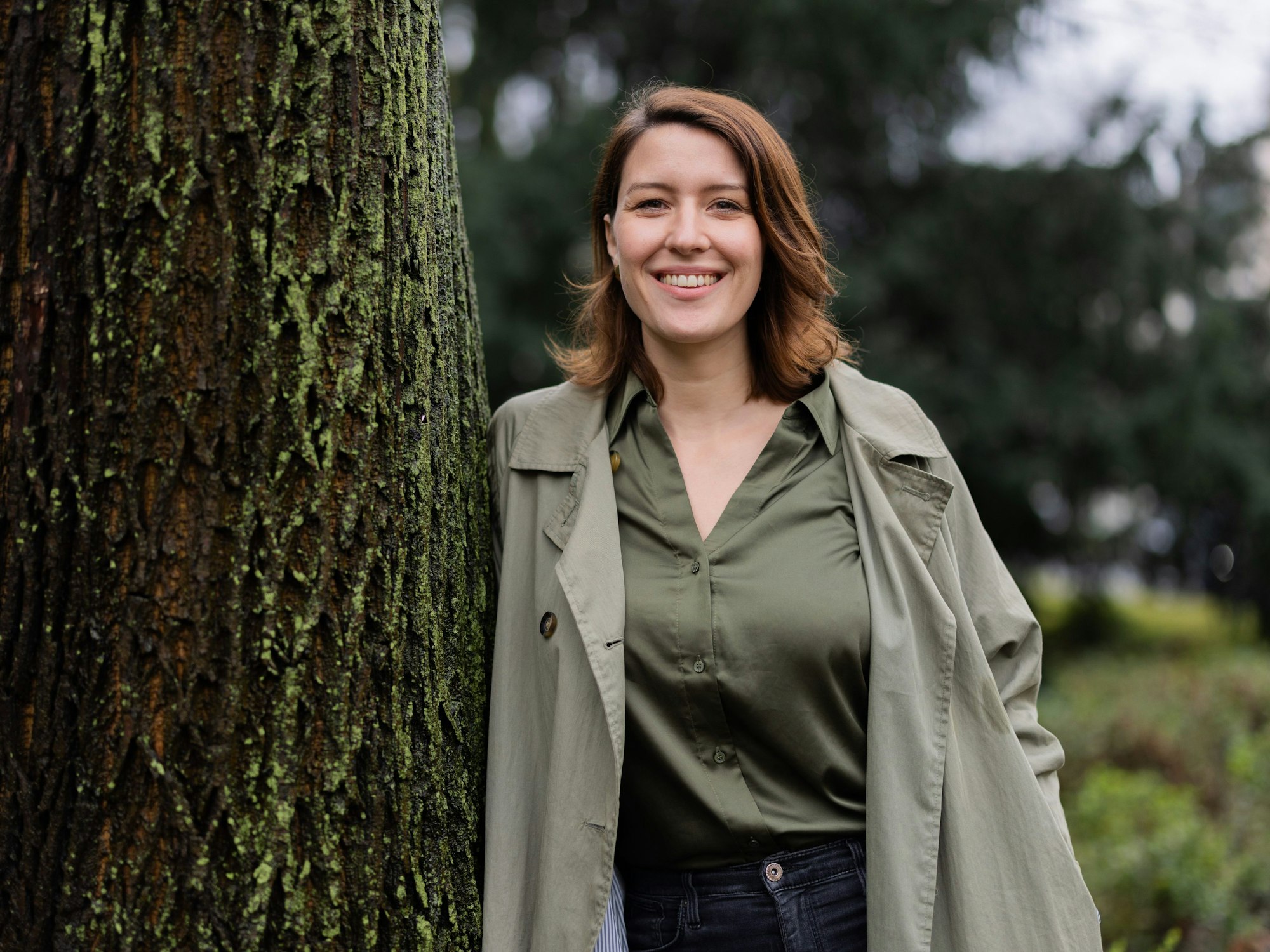 Moderatorin Hannah Emde lehnt bei einem Fotoshooting an einem Baum und lächelt in die Kamera.