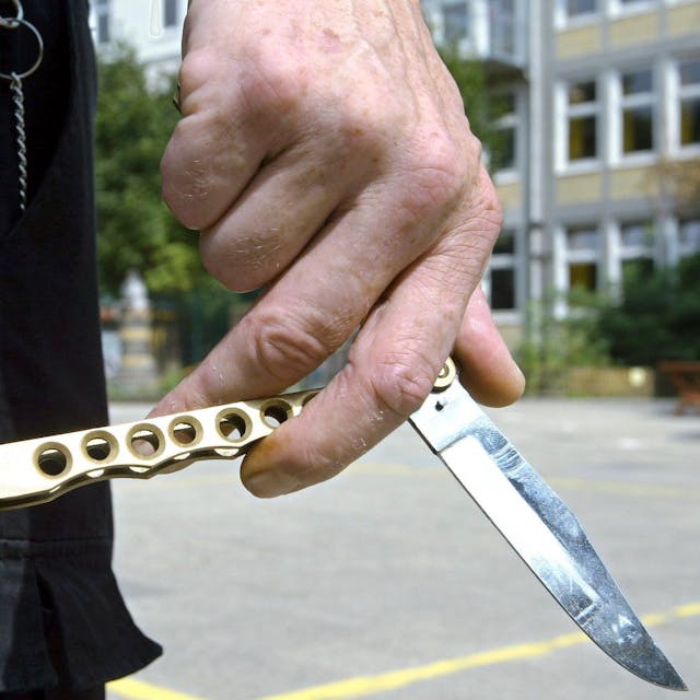 Ein Mann hält auf dem Hof einer Schule ein sogenanntes Butterflymesser in seiner Hand.