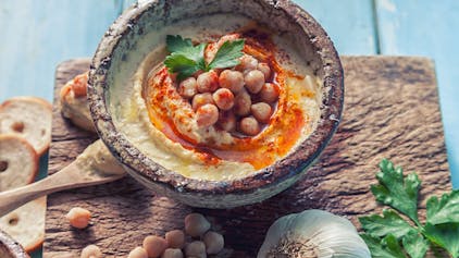 Schale mit Hummus, dekoriert mit Kichererbsen, Petersilie und Paprikapulver