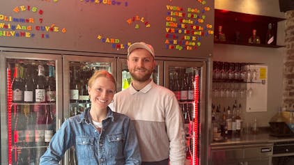 Ein junger Mann und eine junge Frau stehen hinter einer Bar und lächeln