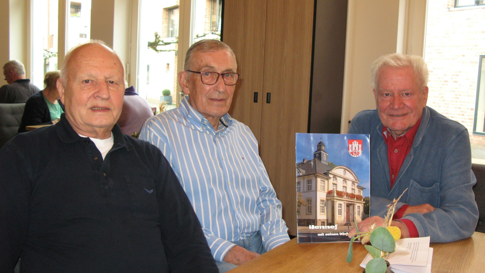 Die drei Männer Karlheinz Becker, Hans-Georg Jülichmanns und Norbert Maibaum, 78, 81 und 81 Jahre alt, sitzen an einem Tisch. Einer hält das Heft mit dem Titel „Hennef mit seinen Dörfern“ in der Hand