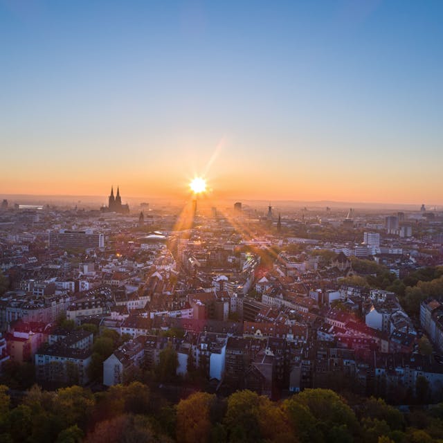 Die Sonne geht an einem wolkenlosen Morgen mit blauem Himmel neben dem Kölner Dom (Hohe Domkirche St. Petrus) über dem Stadtzentrum auf.&nbsp;