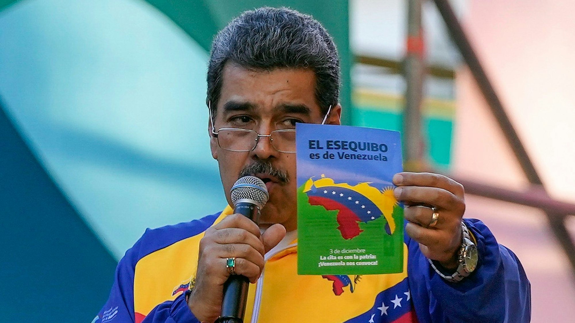 Venezuelas Präsident Nicolás Madurospricht in ein Mikrofon, während er einen Flyer hochhält.