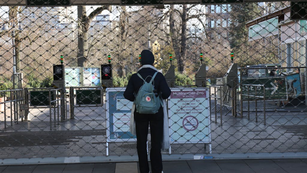 Ein Mann steht am Eingang des Kölner Zoos, der allerdings mit einem großen Gitter verschlossen ist.