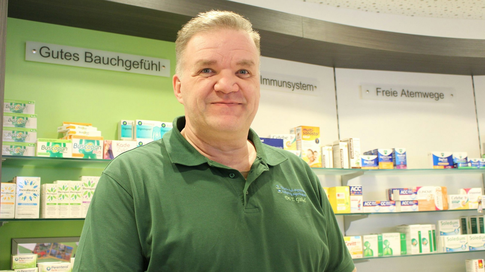 Dr. Thomas Göbel in seiner Apotheke, hinter ihm sind Regale mit Medikamenten zu sehen.