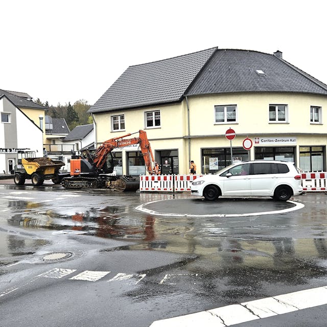 Ein Bagger ist am Kreisverkehr Aachener Straße/Bahnhofstraße im Einsatz. Ein weißes Auto fährt an der Baustelle vorbei.