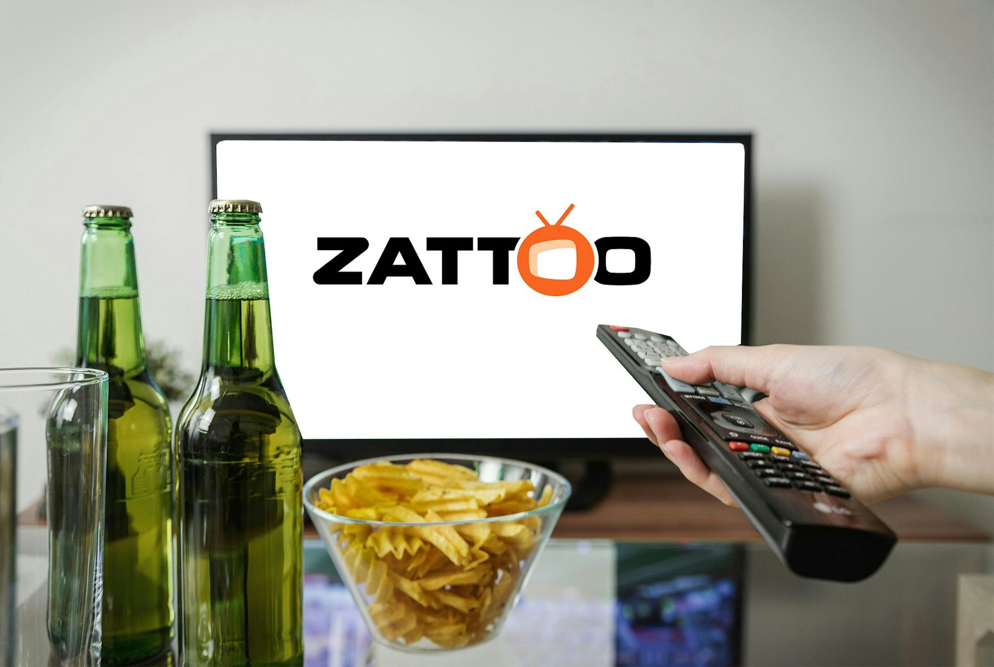 Fernseher mit Zattoo Logo. Im Vordergrund zwei Bierflaschen, eine Fernbedienung und Chips.
