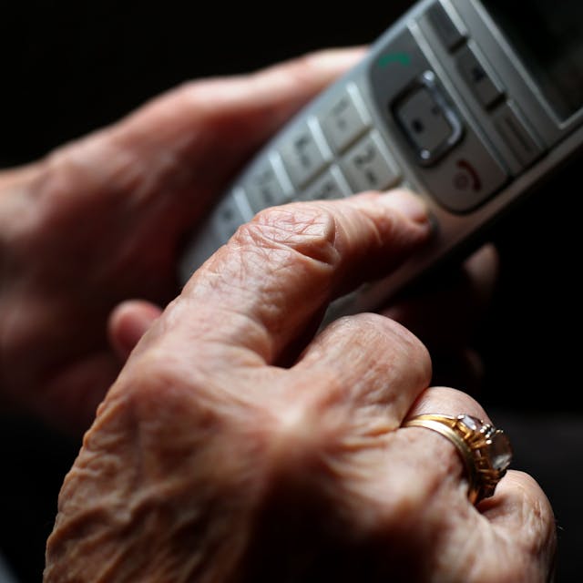 Eine ältere Frau tippt auf einem schnurlosen Festnetztelefon.