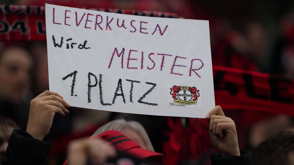 Ein Fan von Bayer Leverkusen hält ein Schild in die Luft, auf dem steht: Leverkusen wird Meister 1. Platz.