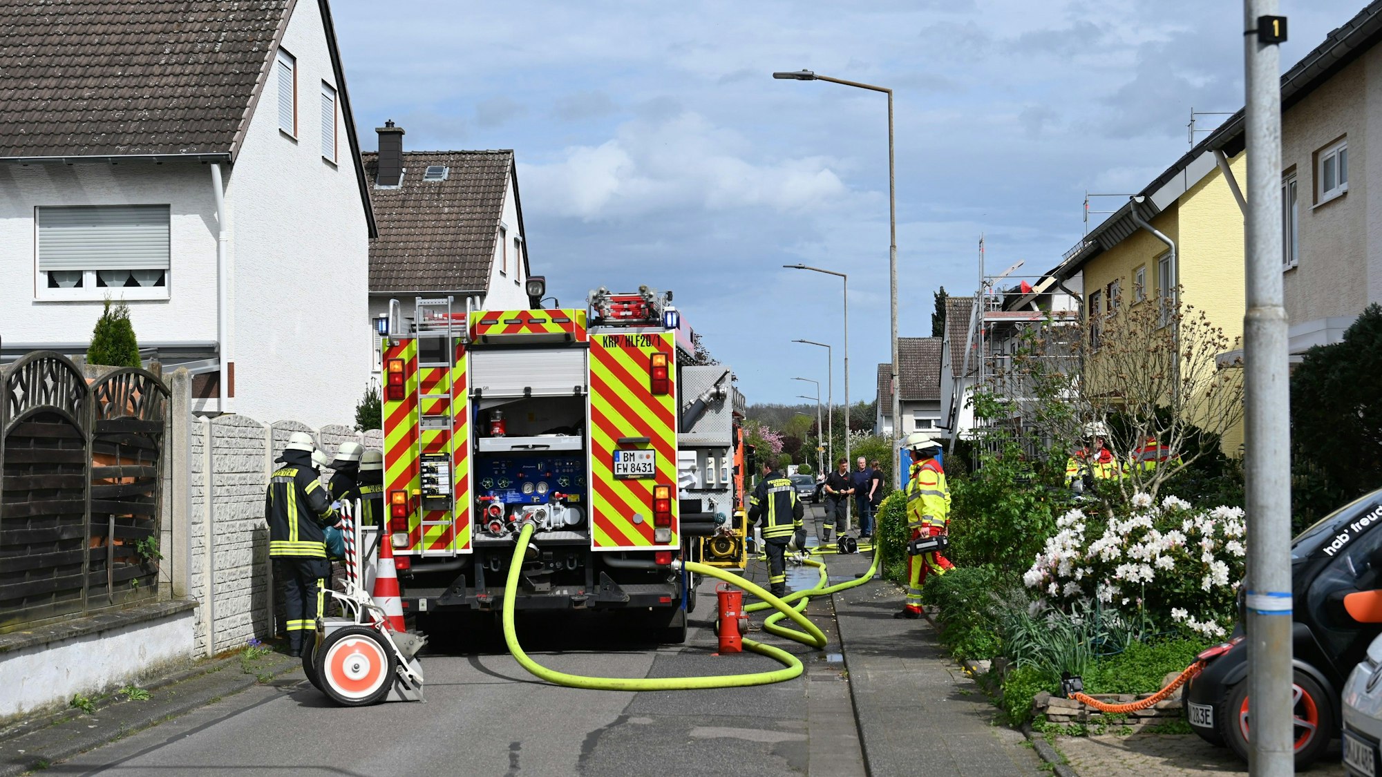 Löschfahrzeuge stehen in einer Wohnstraße in Kerpen Sindorf. Feuerwehrleute rollen gerade die Schläuche wieder zusammen.