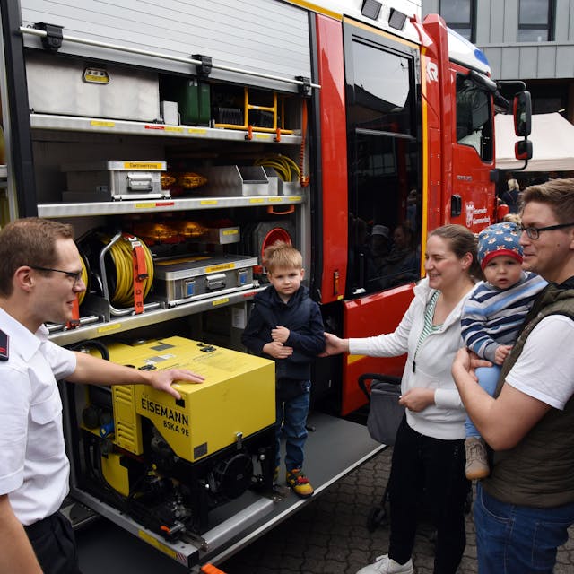 Ein Feuerwehrmann erläutert einer jungen Familie die Ladung eines Feuerwehrautos.