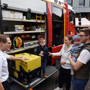 Ein Feuerwehrmann erläutert einer jungen Familie die Ladung eines Feuerwehrautos.
