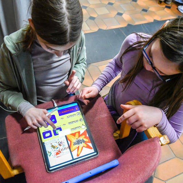Zu sehen sind zwei Kinder, die am Tablet-PC einen Comic erstellen.