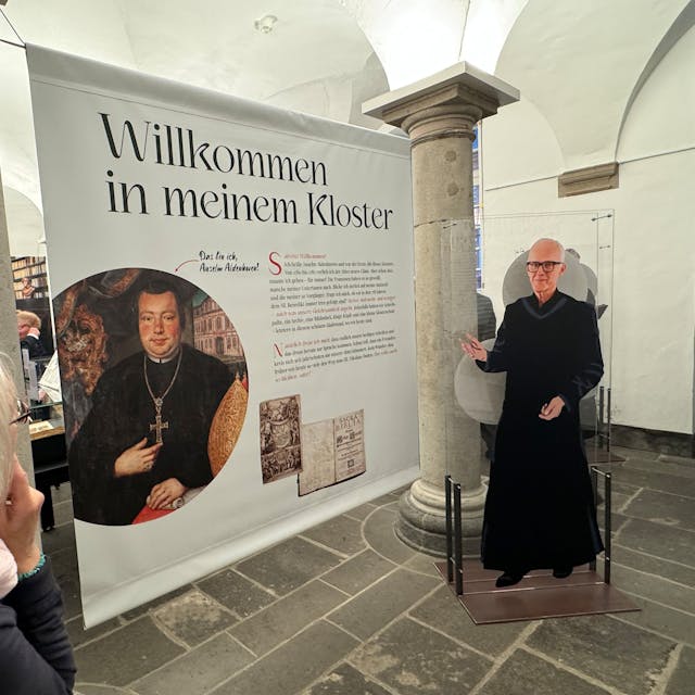 Zu sehen ist eine große Schautafel neben der eine Pappfigur Jürgen Rüttgers in Mönchsgewand zeigt.
