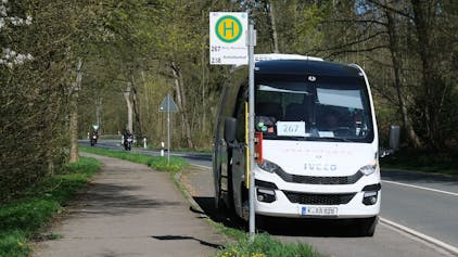 Der weiße Kleinbus steht an einer Haltestelle an einer Landstraße.