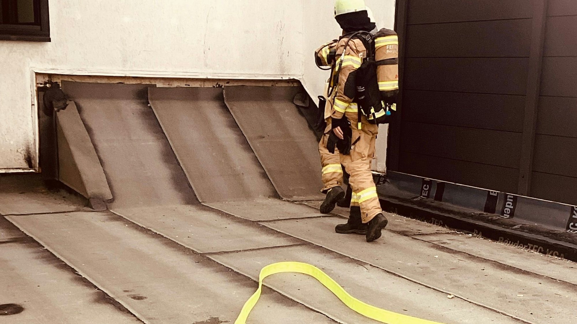 Zwei Feuerwehrleute stehen auf einem mit Dachpappe gedeckten Dach.