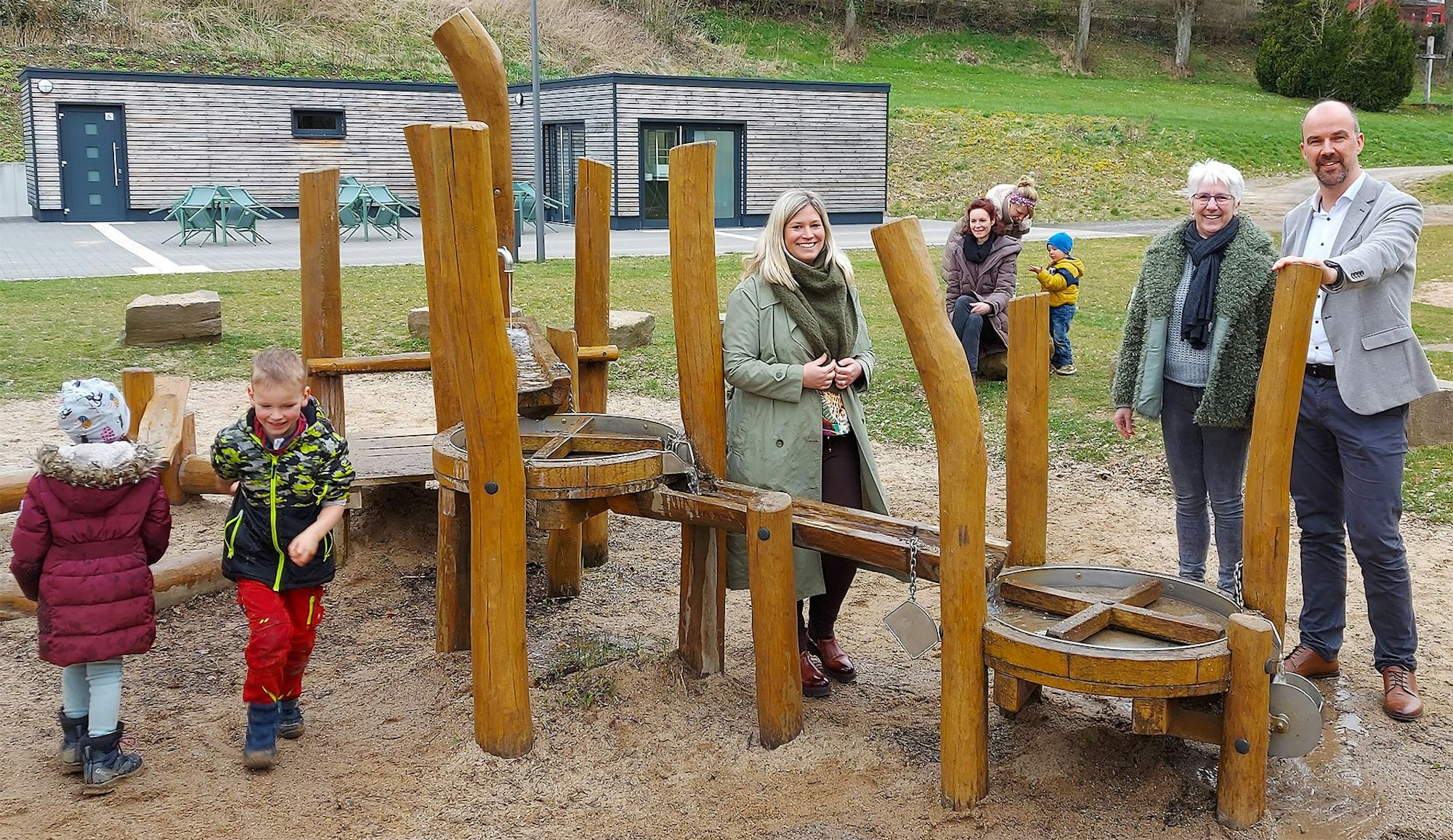 Bürgermeisterin Jennifer Meuren, Annegret Dreimüller und Guido Waters stehen am Kleinkinderspielplatz. Einige Kinder spielen.