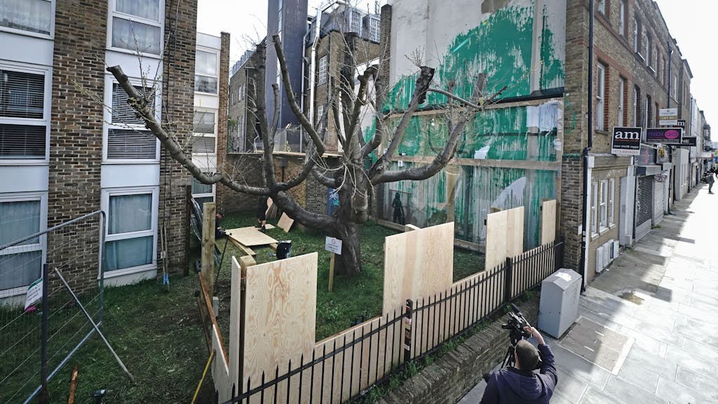 Neben dem Banksy-Kunstwerk an der Seite eines Wohnhauses in der Hornsey Road in Finsbury Park im Norden Londons, das zum Schutz mit einer Plexiglasscheibe abgedeckt wurde, wird eine Holzwand angebracht.