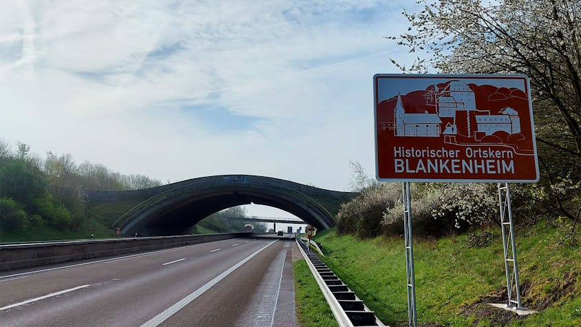 Am rechten Fahrbahnrand steht das neue Schild, auf dem zu lesen ist: „Historischer Ortskern Blankenheim“. Im Hintergrund ist die Wildbrücke zu sehen.