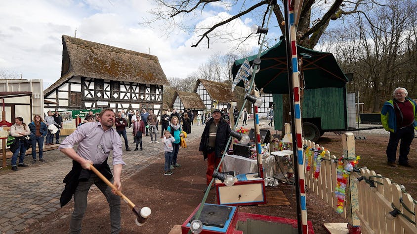 Ein Besucher des historischen Jahrmarkts schwingt den Hammer beim „Hau den Lukas“. Im Hintergrund stehen Fachwerkhäuser.