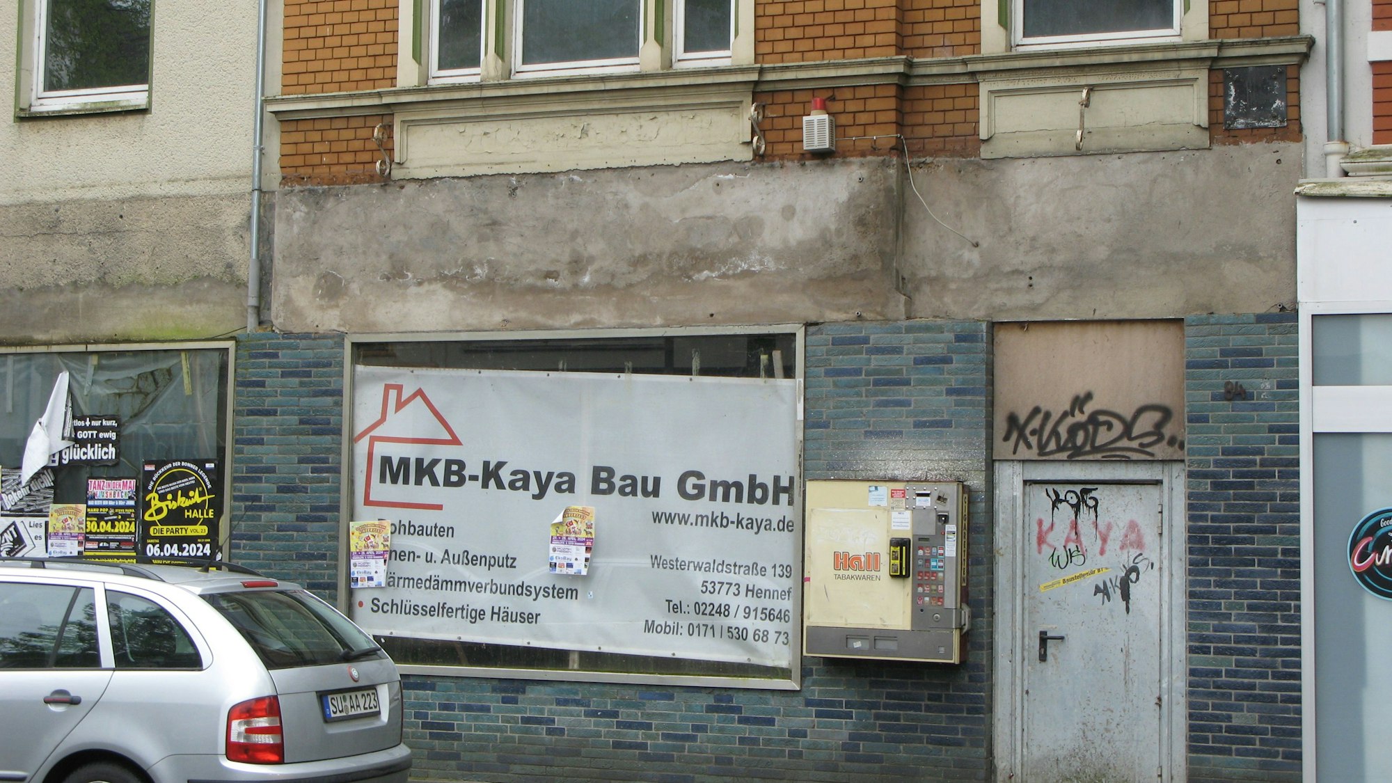 Das Bild zeigt eine verwahrlost wirkende Fassade in der Hennefer Innenstadt mit zugehängten und zuplakatierten Schaufenstern und Farbschmierereien.