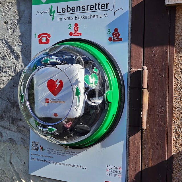 Das Bild zeigt einen Defibrillator, der an einer Wand angebracht ist.