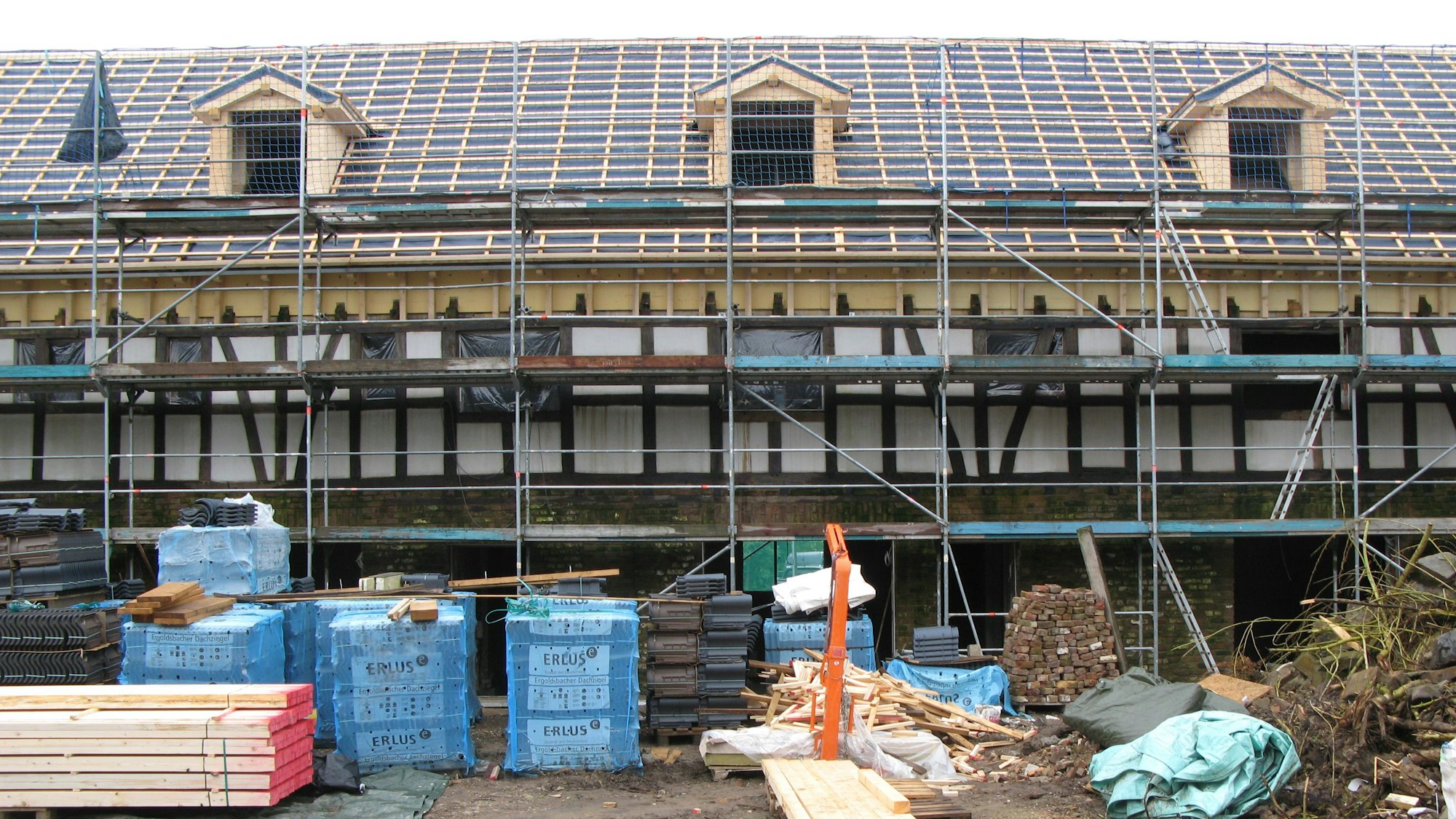 Ein langgestrecktes Fachwerkgebäude ist eingerüstet, das Dach ist für die Neueindeckung vorbereitet.