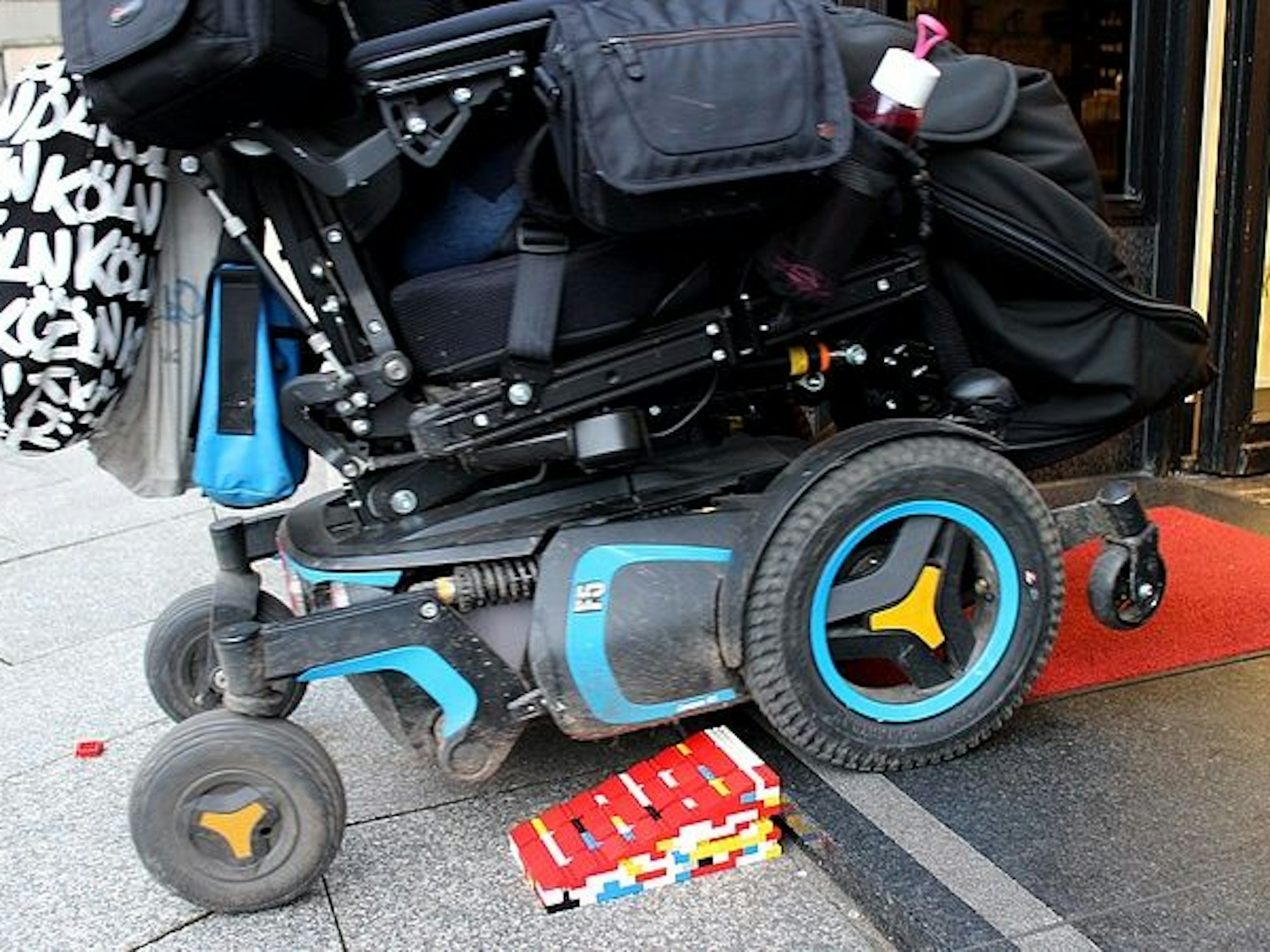 Ein Rollstuhl fährt über eine Legorampe in ein Geschäft.
