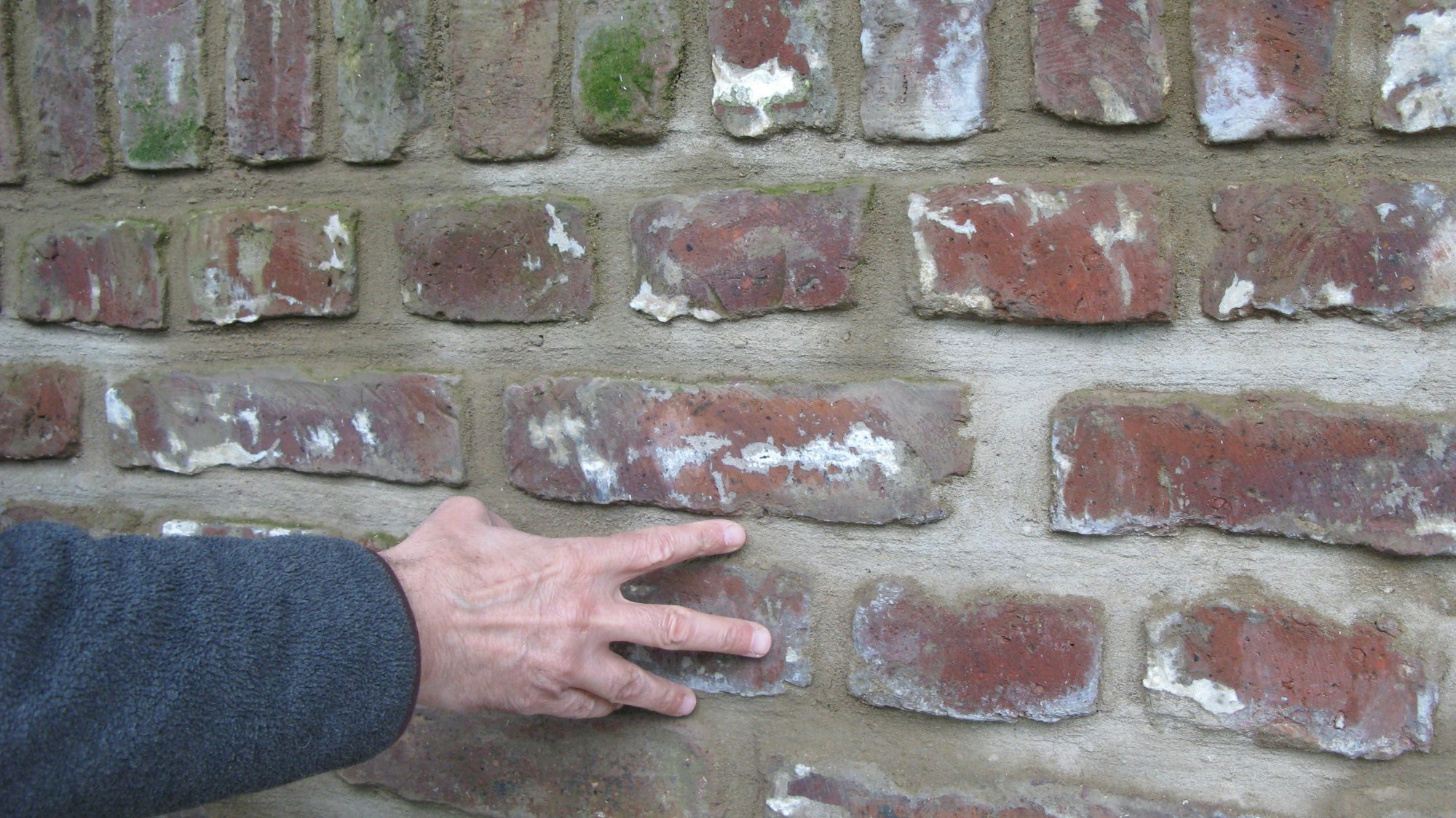Eine Hand liegt auf einer sanierten neu verfugten Ziegelsteinmauer.