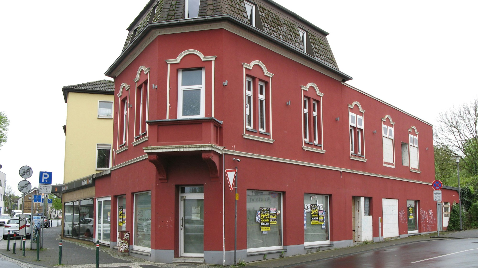 Das Foto zeigt ein rotes Eckhaus mit leeren und teils zugemauerten Schaufenstern.