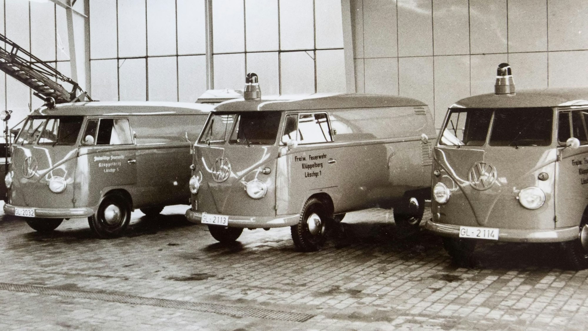 Schwarzweißbild von VW-Bullis mit Blaulicht, die 1962 in einer Halle in einer Reihe stehen.