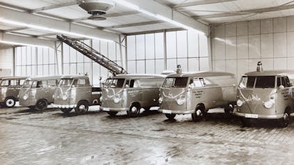 Schwarzweißbild von VW-Bullis mit Blaulicht, die 1962 in einer Halle in einer Reihe stehen.