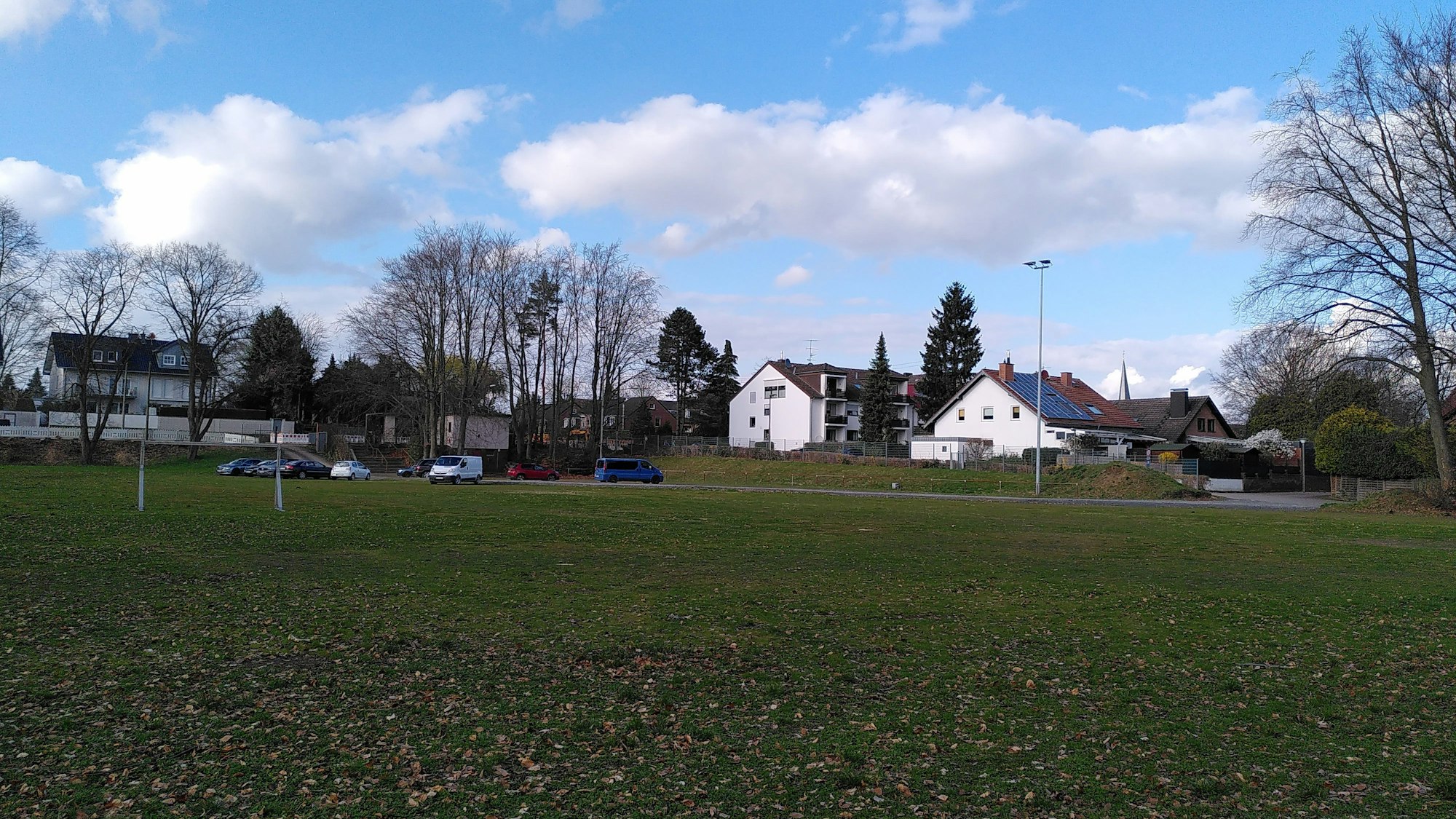 Im Vordergrund ist ein Sportplatz zu sehen, im Hintergrund stehen Wohnhäuser.