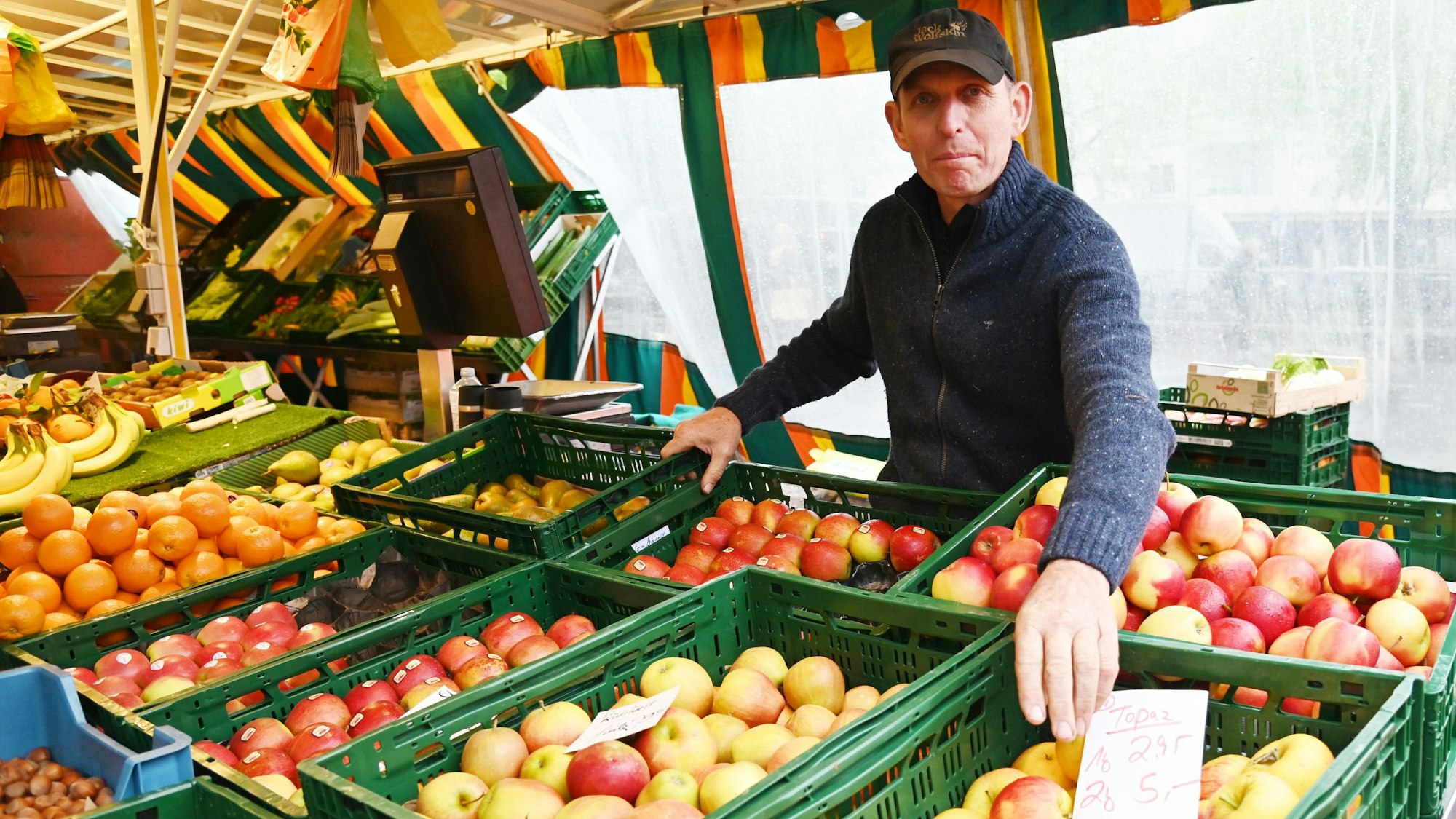 Lebensmittelhändler Theo Aßenmacher steht an seinem Stand und präsentiert Boxen voller Äpfel. Foto von Alexander Schwaiger

