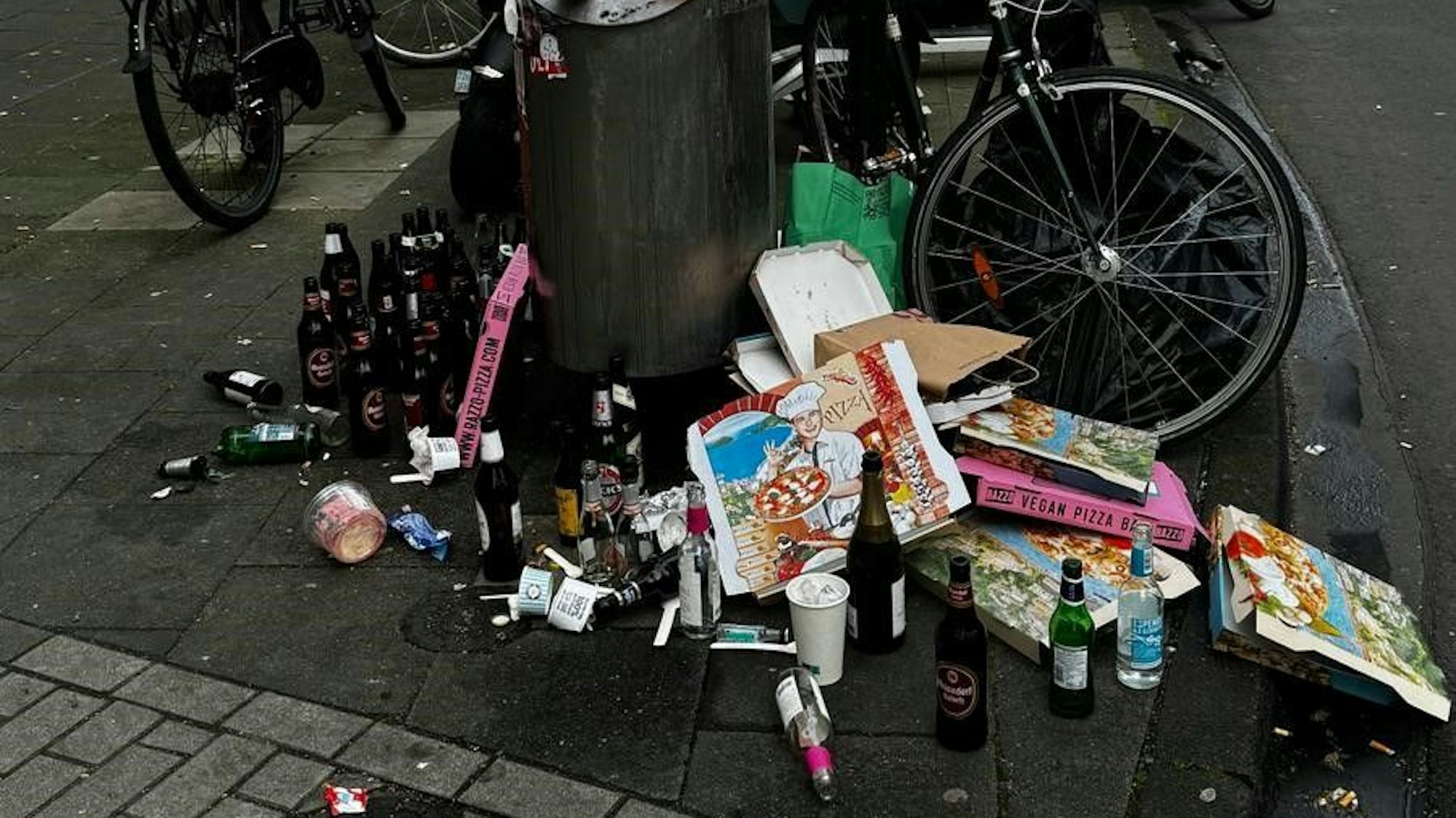 Vor einem Mülleimer liegen leere Pizzakartons und Bierflaschen.