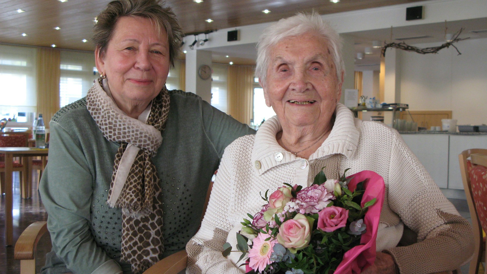 Die 102 Jahre alte Charlotte Seeger sitzt mit einem Blumenstrauß in den Händen neben ihrer 74-jährigen Tochter.