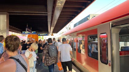 Ein Zug der S-Bahnlinie 11 hält im Sommer an einem vollen Bahnsteig in Köln.