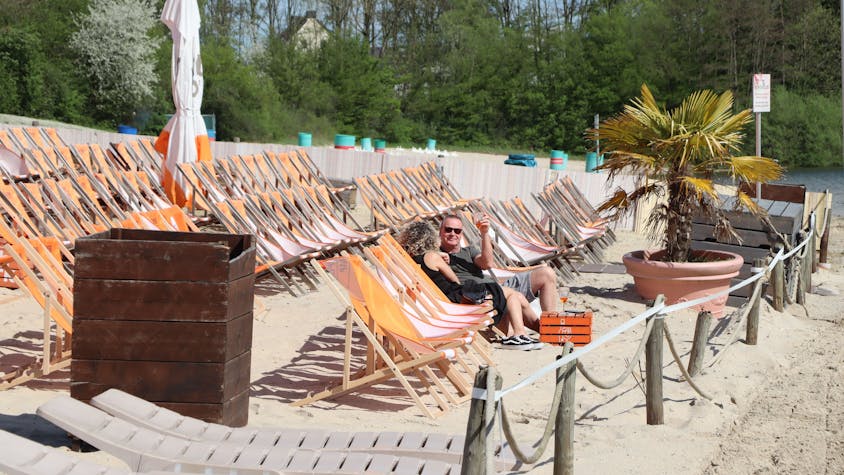Eine Reihe von Liegestühlen am Sandstrand des Otto-Maigler-Sees. Zwei Besucher genießen schon die Sonne.